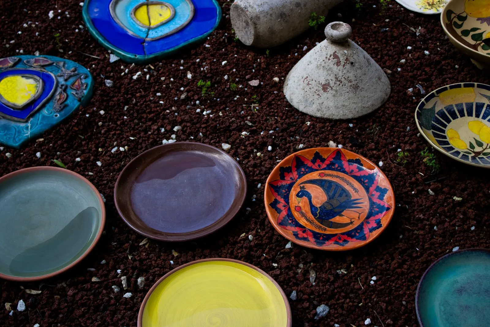 Various handcrafted ceramic plates in vibrant colors and patterns laid out on a textured surface.